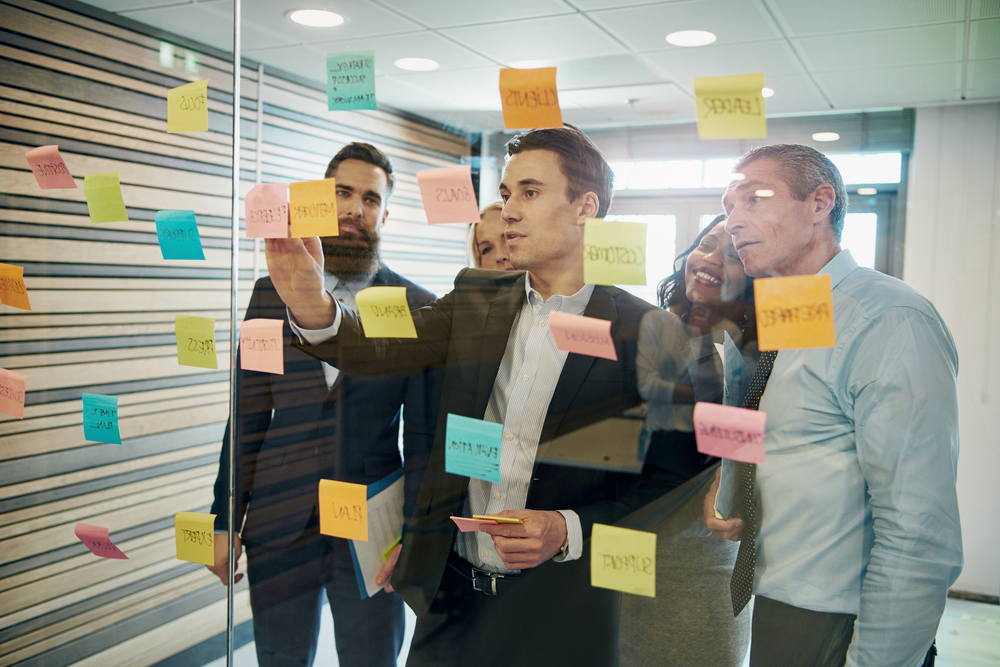 group of people in business attire, having a discussion and pasting post it notes on glass